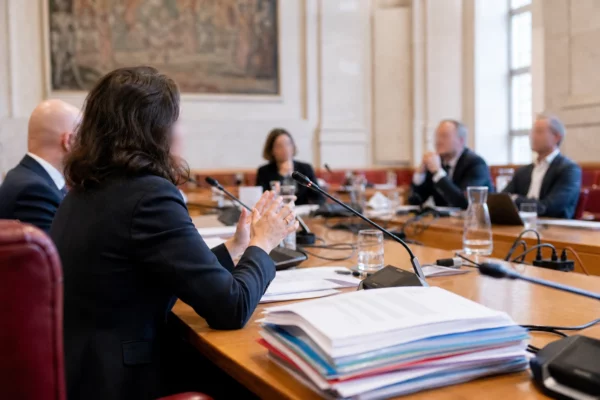 Réunion de commission parlementaire en France avec micros, dossiers ouverts et silhouettes anonymes autour d’une table.