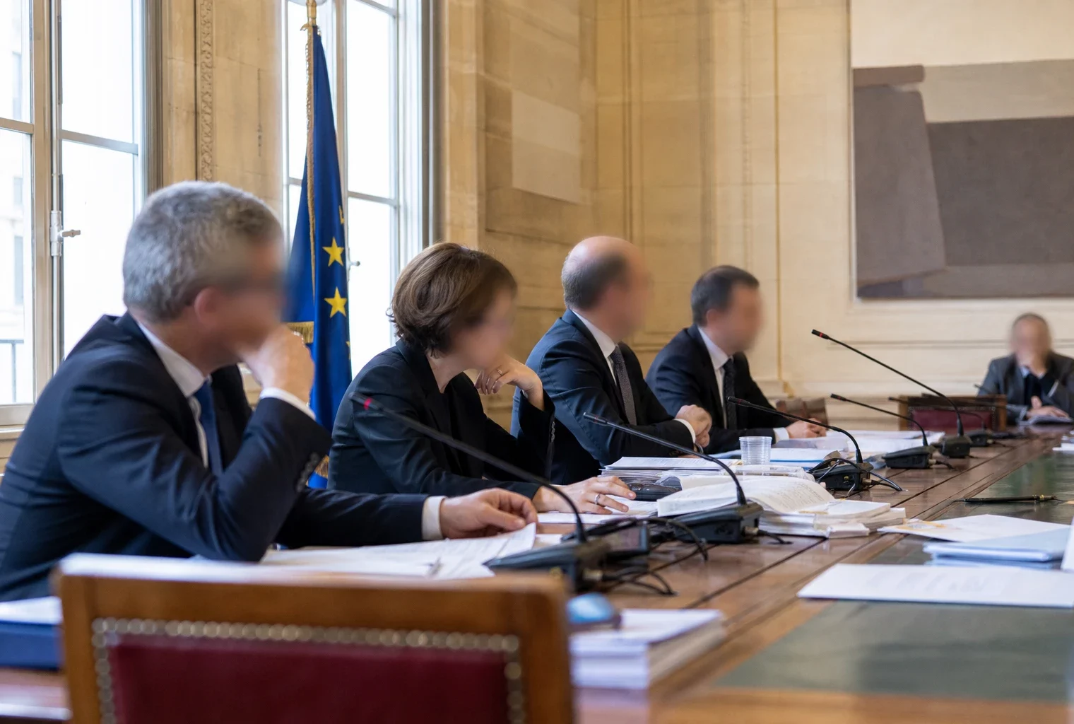 Réunion de commission parlementaire avec micros, dossiers ouverts et silhouettes anonymes dans une salle lumineuse.