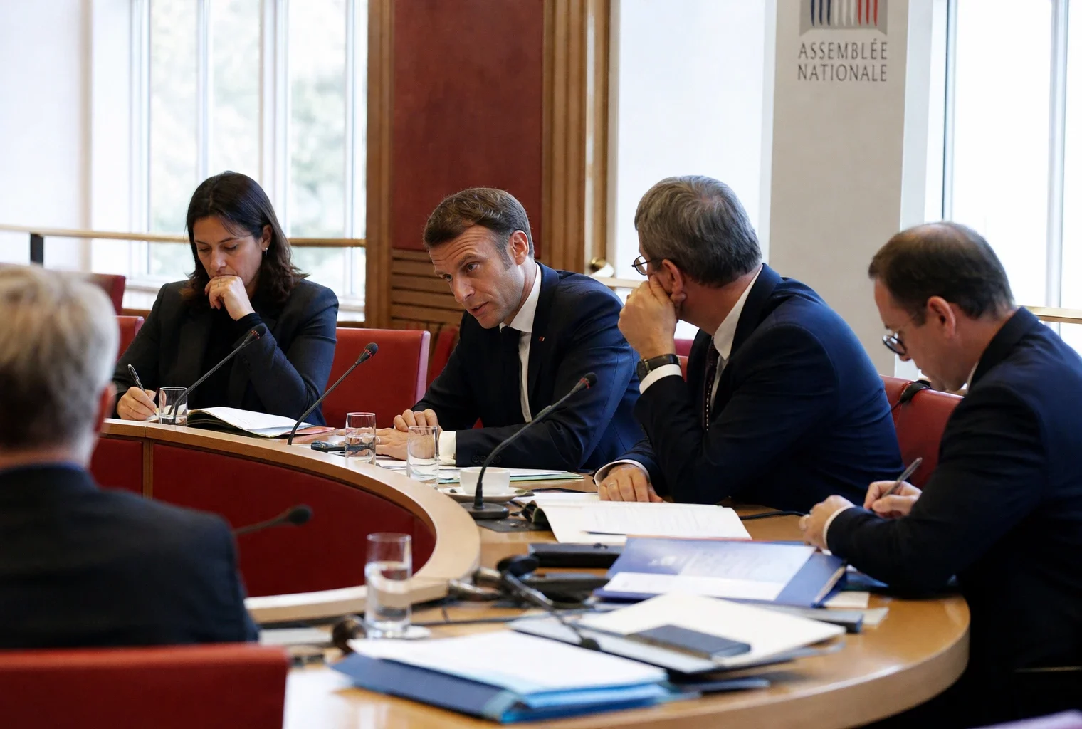 Réunion parlementaire en commission avec plusieurs élus anonymes, micros, dossiers ouverts et lumière naturelle claire.