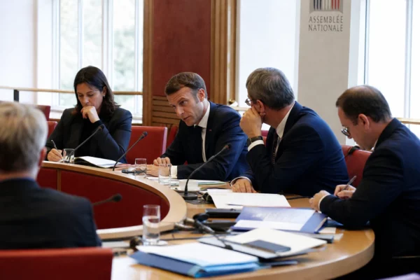 Réunion parlementaire en commission avec plusieurs élus anonymes, micros, dossiers ouverts et lumière naturelle claire.
