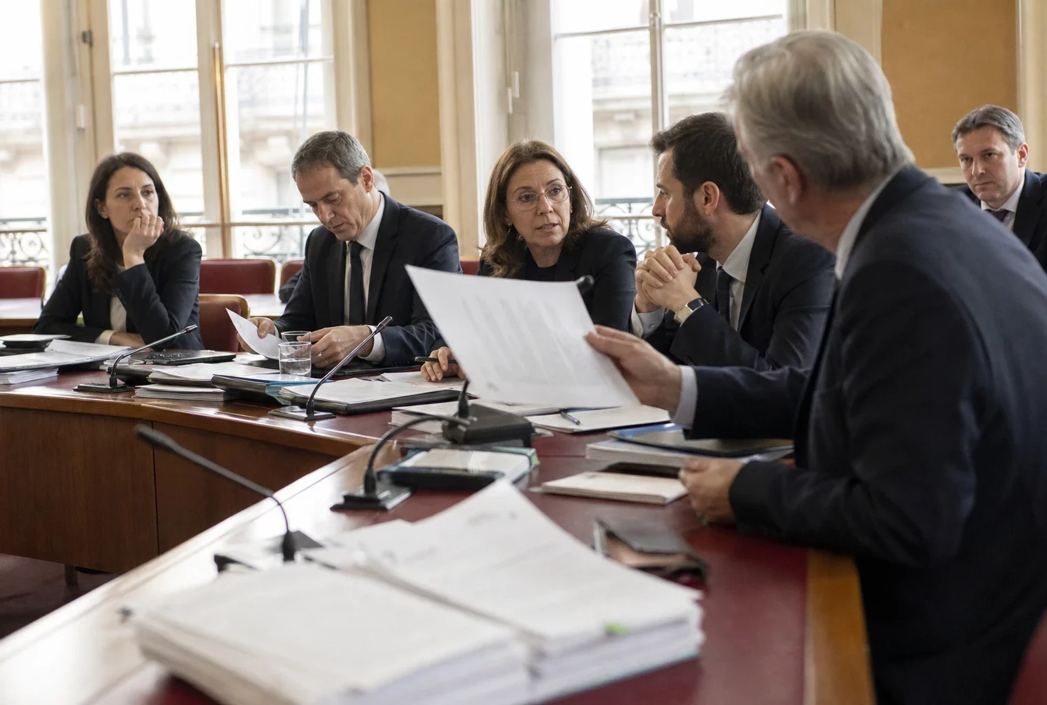 Réunion parlementaire en commission avec députés anonymes, micros et dossiers autour d’une table