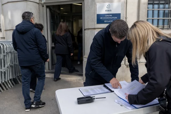 Agent de sécurité et documents d’autorisation devant un bâtiment administratif parisien, en scène de terrain calme.