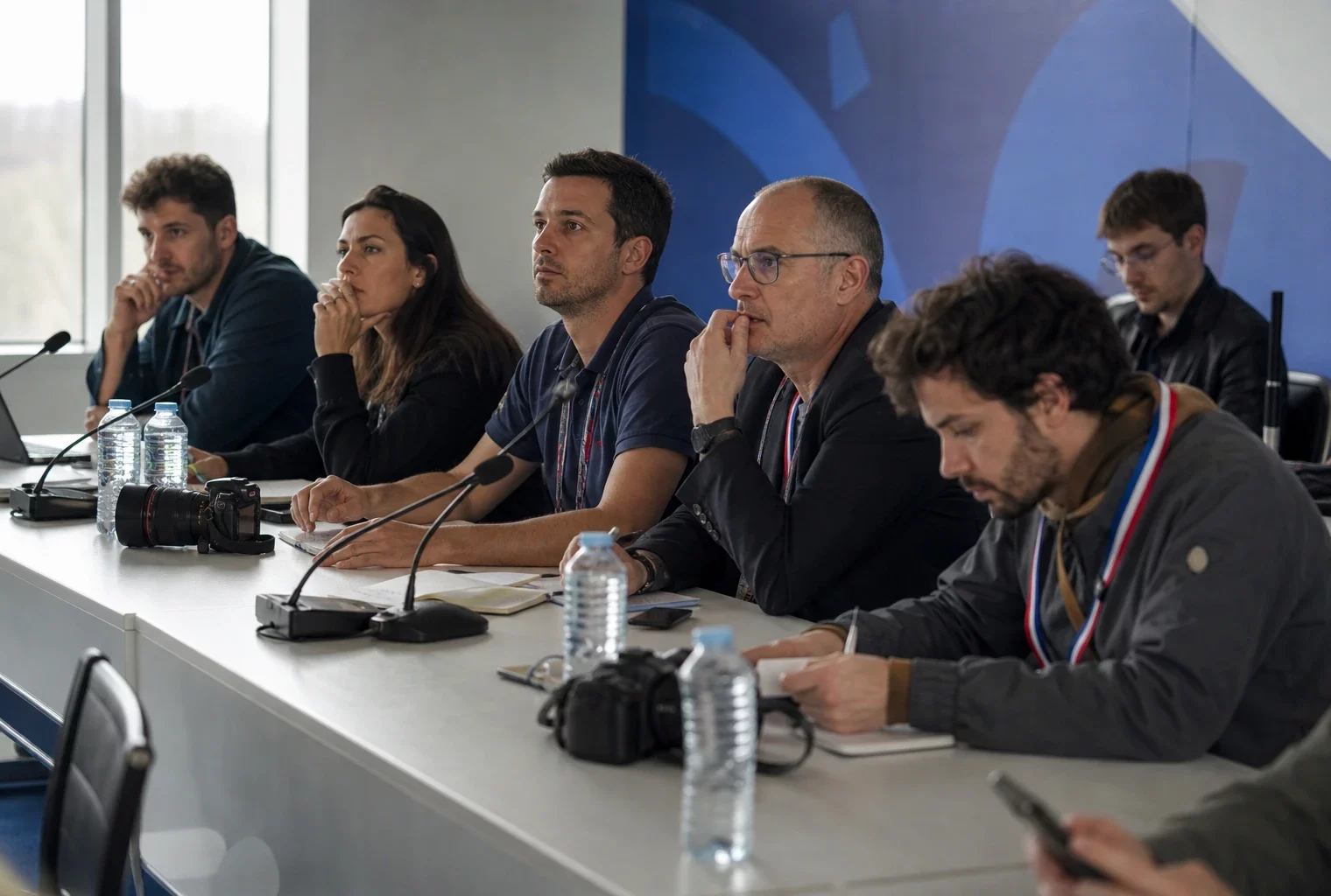 Conférence de presse du Mondial avec plusieurs journalistes anonymes, micros et carnets dans une salle lumineuse.