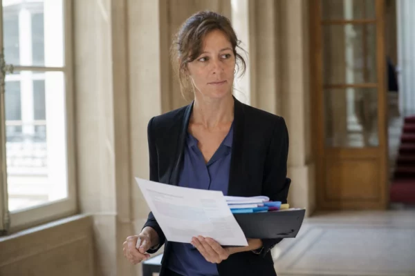 Portrait d’un haut fonctionnaire français dans un couloir ministériel lumineux, dossier à la main, ambiance estivale discrète.