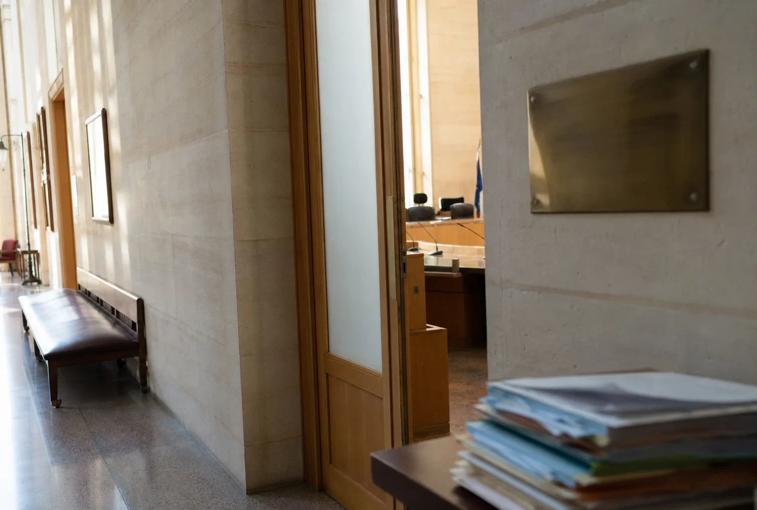 Couloir lumineux d’une institution française avec porte sobre et salle d’audition en arrière-plan.