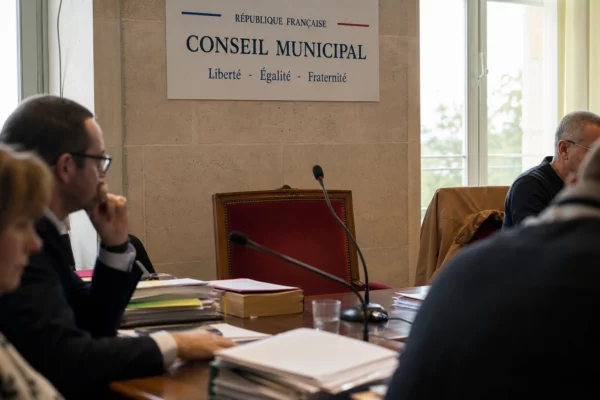 Salle municipale lumineuse avec chaise vide, micros et dossiers flous pour illustrer le débat agricole.