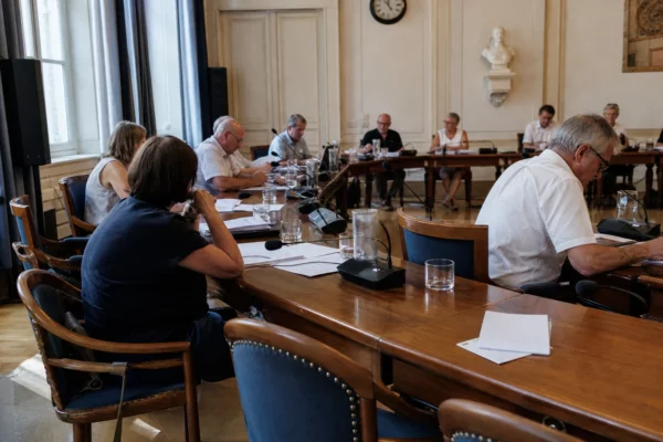 Salle municipale de conseil local avec micros, dossiers et une chaise vide lors d’une réunion sur la canicule