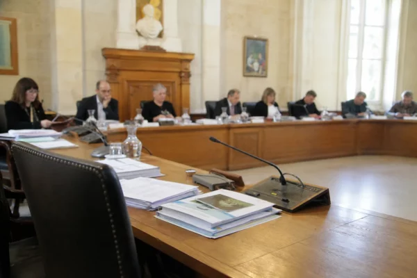 Salle municipale avec micros, dossiers flous et chaise vide lors d’une réunion sur l’eau