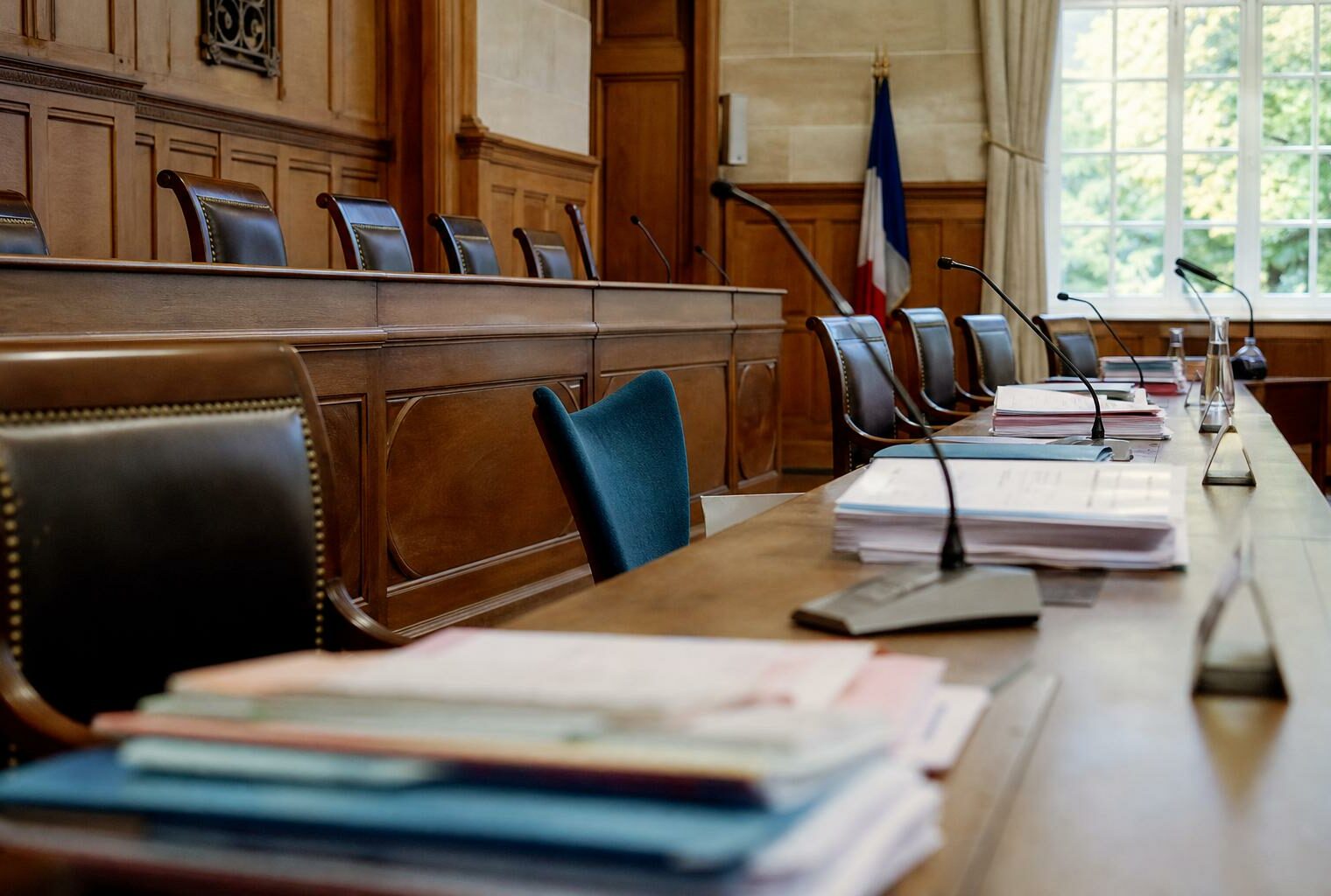 Salle du conseil municipal française avec chaise vide, micros et dossiers flous dans une lumière naturelle claire