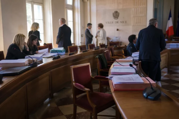 Salle municipale lumineuse avec chaises vides, micros et dossiers flous lors d’un conseil local à Nice