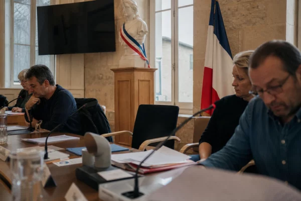 Salle municipale française avec chaise vide, micros et dossiers flous, dans une lumière naturelle claire.