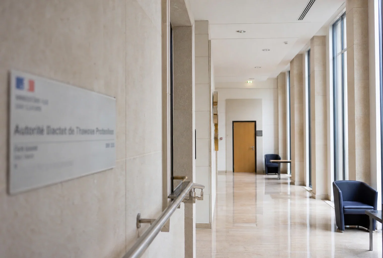 Couloir clair d’un bâtiment institutionnel français menant à une salle d’audition vide