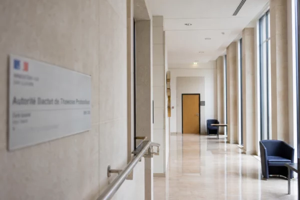 Couloir clair d’un bâtiment institutionnel français menant à une salle d’audition vide