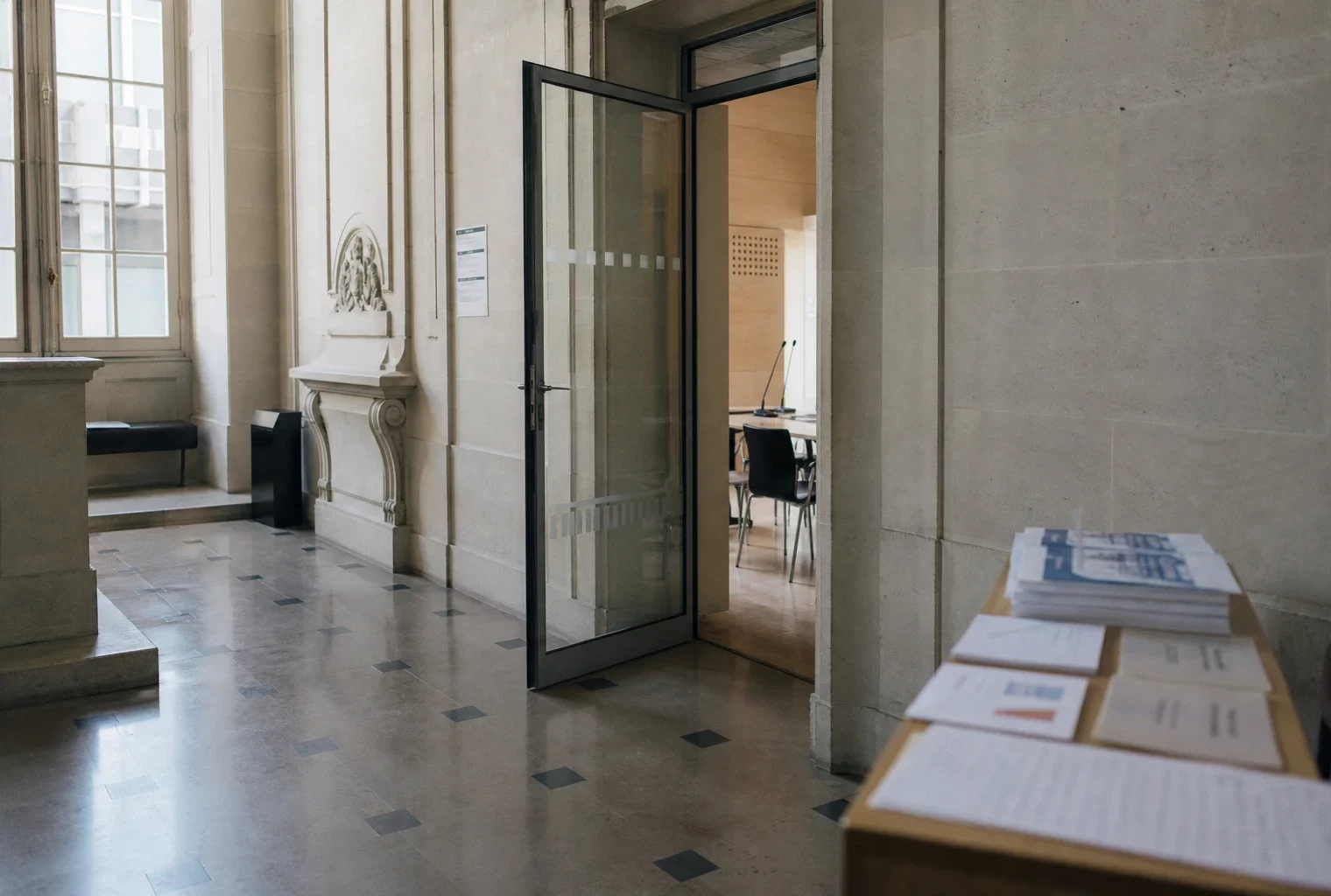 Couloir lumineux d’un bâtiment institutionnel français avec porte ouverte vers une salle d’audition vide.