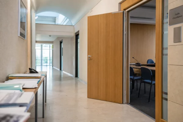 Couloir clair d’un lieu institutionnel français avec salle d’audition sobre et ambiance documentaire