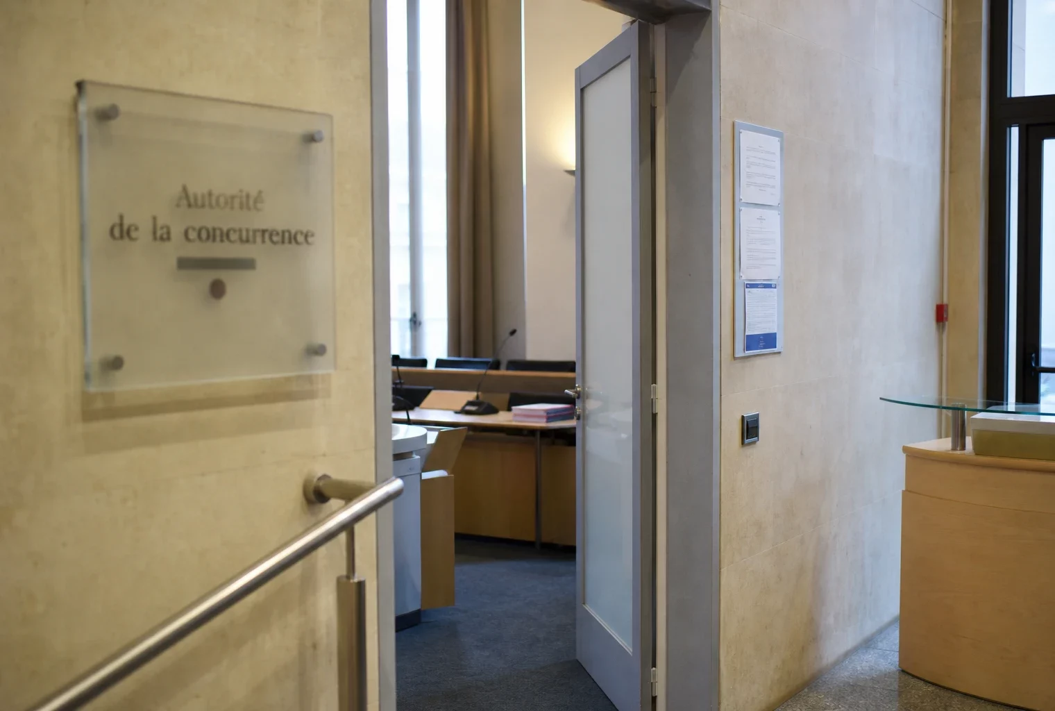 Couloir clair d’un bâtiment institutionnel français menant à une salle d’audition, avec porte entrouverte et dossiers flous.