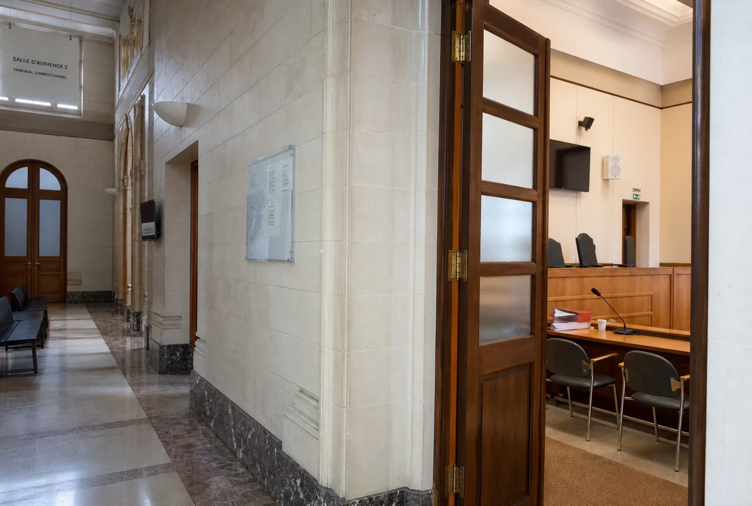 Couloir clair d’une institution judiciaire avec porte sobre et salle d’audition visible au fond.