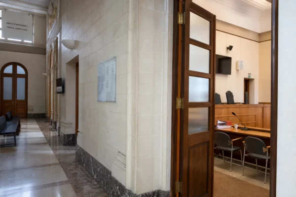 Couloir clair d’une institution judiciaire avec porte sobre et salle d’audition visible au fond.