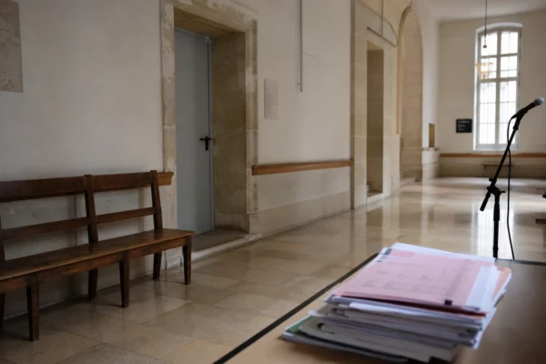 Couloir clair d’un bâtiment institutionnel français avec porte sobre, lumière naturelle et dossiers anonymes.
