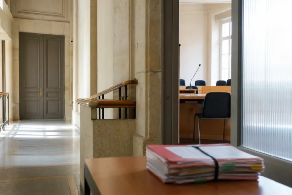 Couloir lumineux d’une institution publique française avec salle d’audition sobre et dossiers flous sur une table.