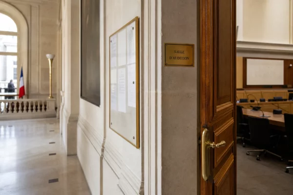 Couloir clair d’un bâtiment institutionnel avec porte d’audition entrouverte et signalétique floue