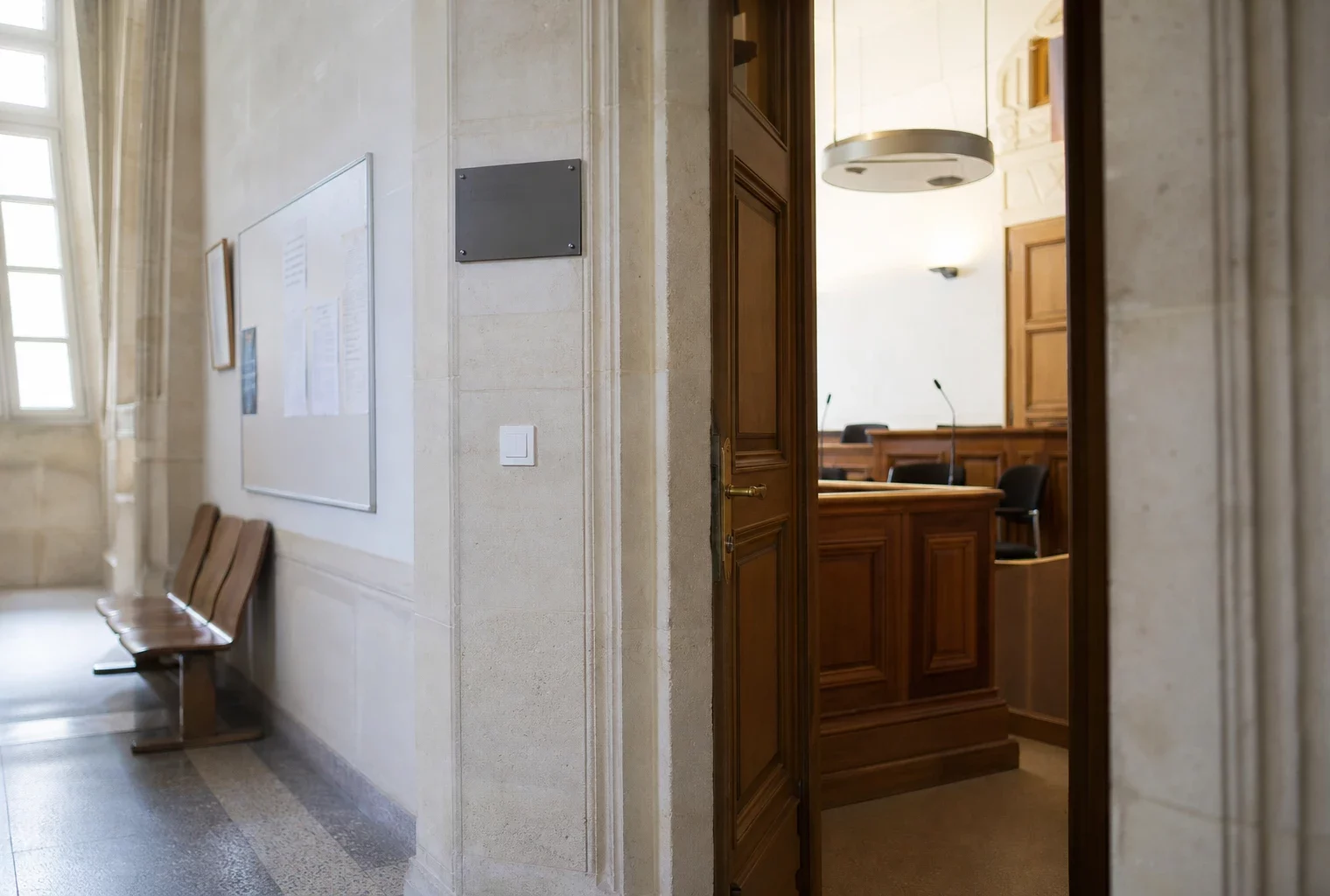 Couloir clair d’un bâtiment institutionnel français, porte sobre et salle d’audition en arrière-plan
