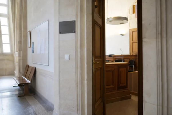 Couloir clair d’un bâtiment institutionnel français, porte sobre et salle d’audition en arrière-plan