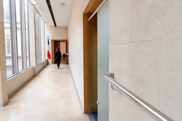 Couloir clair d’un bâtiment institutionnel français, avec porte sobre et salle d’audition en arrière-plan.