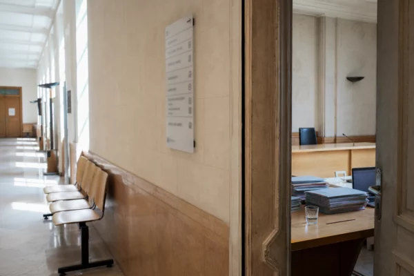 Couloir lumineux d’un bâtiment institutionnel français menant à une salle d’audition, avec portes sobres et dossiers flous.