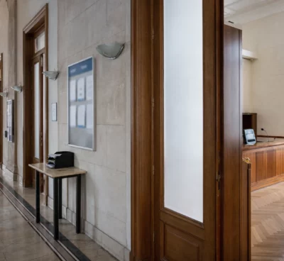 Couloir clair d’un bâtiment institutionnel français, porte entrouverte et salle d’audition en arrière-plan