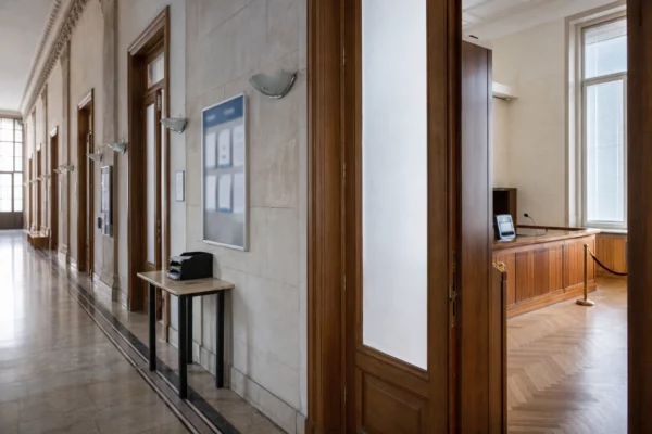 Couloir clair d’un bâtiment institutionnel français, porte entrouverte et salle d’audition en arrière-plan