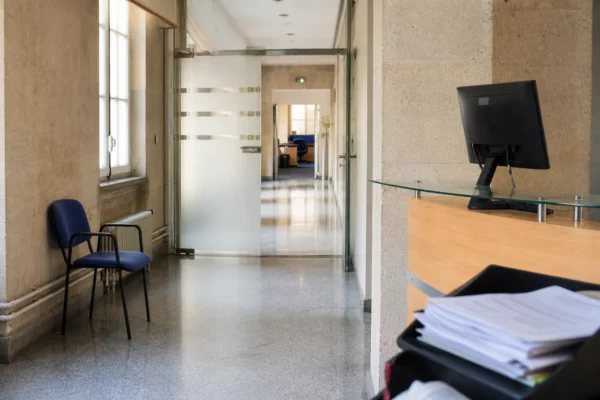 Couloir clair d’un bâtiment institutionnel français, avec porte sobre, bureau vide et documents flous.