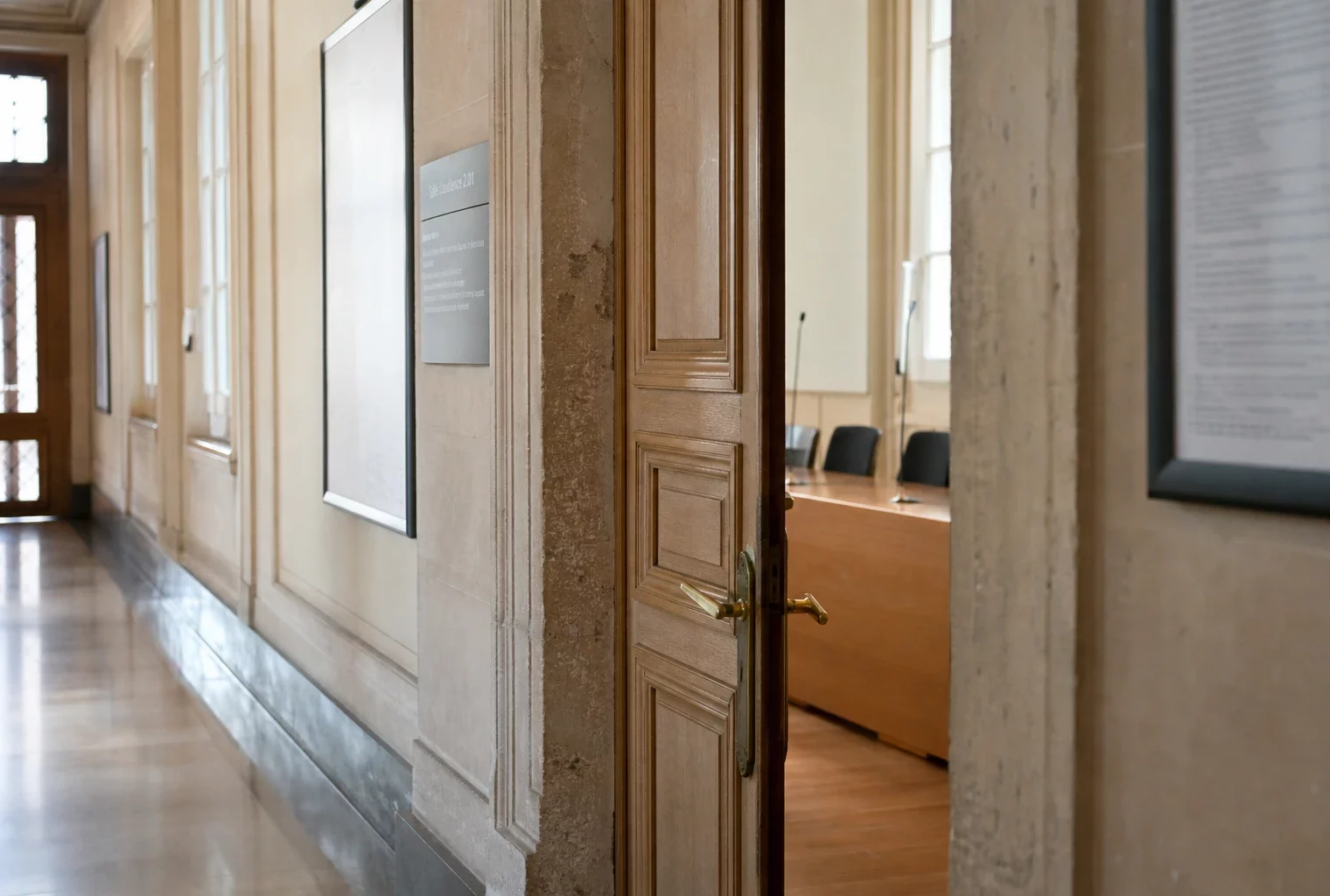 Couloir clair d’un bâtiment institutionnel français, vu en oblique vers une salle d’audition vide.