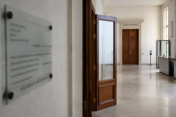 Couloir clair d’un bâtiment institutionnel de justice européenne, avec porte d’audition et lumière naturelle.