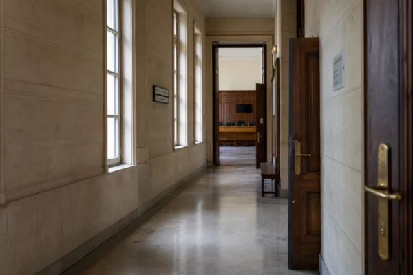 Couloir clair d’un bâtiment judiciaire français, avec porte entrouverte et salle d’audition au fond.