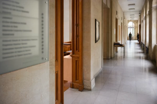 Couloir lumineux d’un bâtiment public français avec porte d’audition entrouverte et ambiance institutionnelle sobre.
