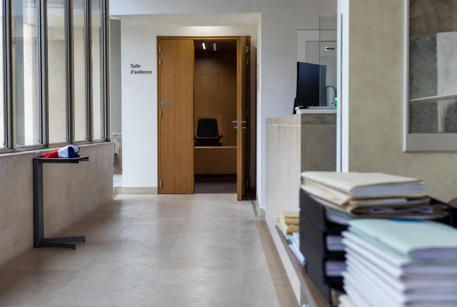 Couloir clair d’un bâtiment institutionnel français avec porte entrouverte et salle d’audition au fond.