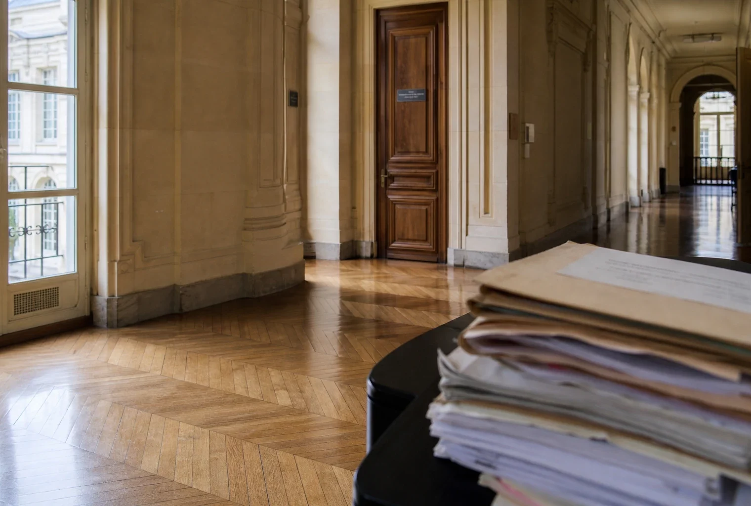 Couloir lumineux d’un bâtiment institutionnel parisien avec dossiers sur une table, ambiance sobre et officielle.