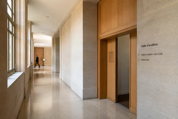 Couloir institutionnel lumineux d’un théâtre public à Strasbourg, vu en oblique avec porte sobre et ambiance officielle calme