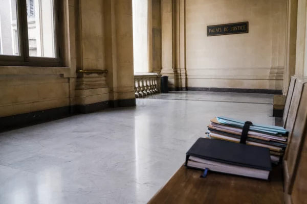 Couloir lumineux d’un palais de justice français avec dossiers flous et plaque institutionnelle en arrière-plan