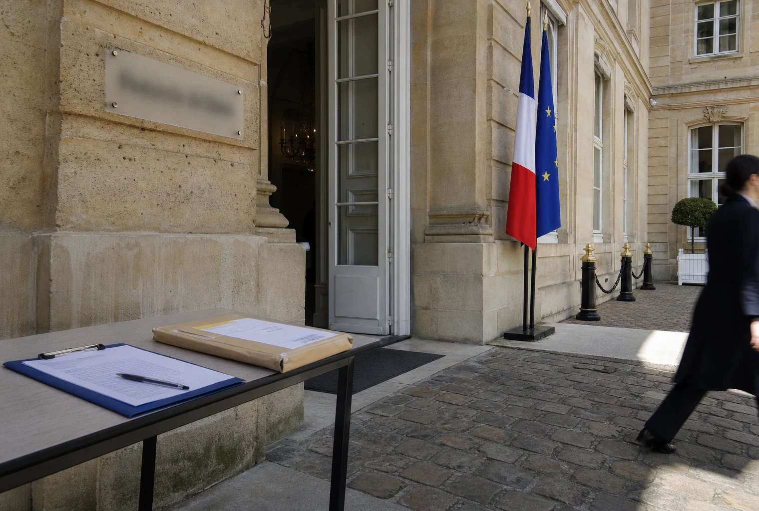 Cour intérieure d’un bâtiment ministériel parisien, avec entrée discrète, plaque institutionnelle floue et agent anonyme au bord du cadre.