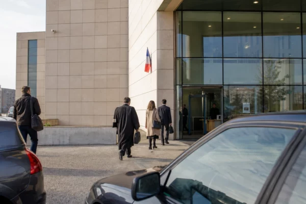 Devant un tribunal français, des silhouettes anonymes circulent dans une ambiance calme et documentaire.
