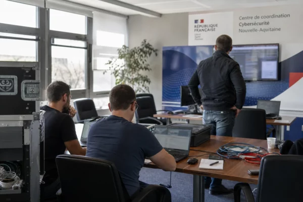 Salle de coordination cyber dans un bâtiment public français, avec techniciens anonymes et écrans flous en pleine activité.