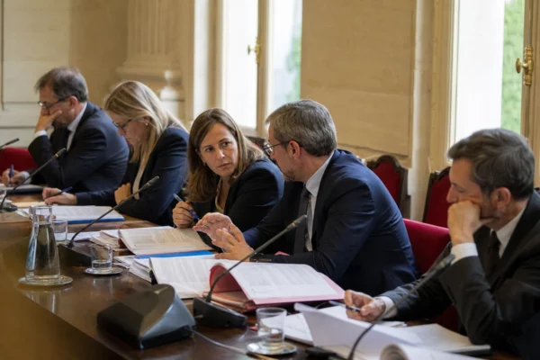 Commission parlementaire française avec micros, dossiers ouverts et cinq personnes discutant de justice en lumière naturelle.