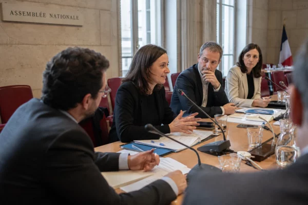 Réunion politique en commission à l’Assemblée nationale avec micros, dossiers et plusieurs personnes anonymes.
