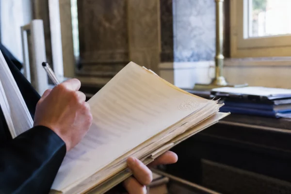 Gros plan d’une main dans un tribunal, annotant un dossier judiciaire sous une lumière naturelle claire.