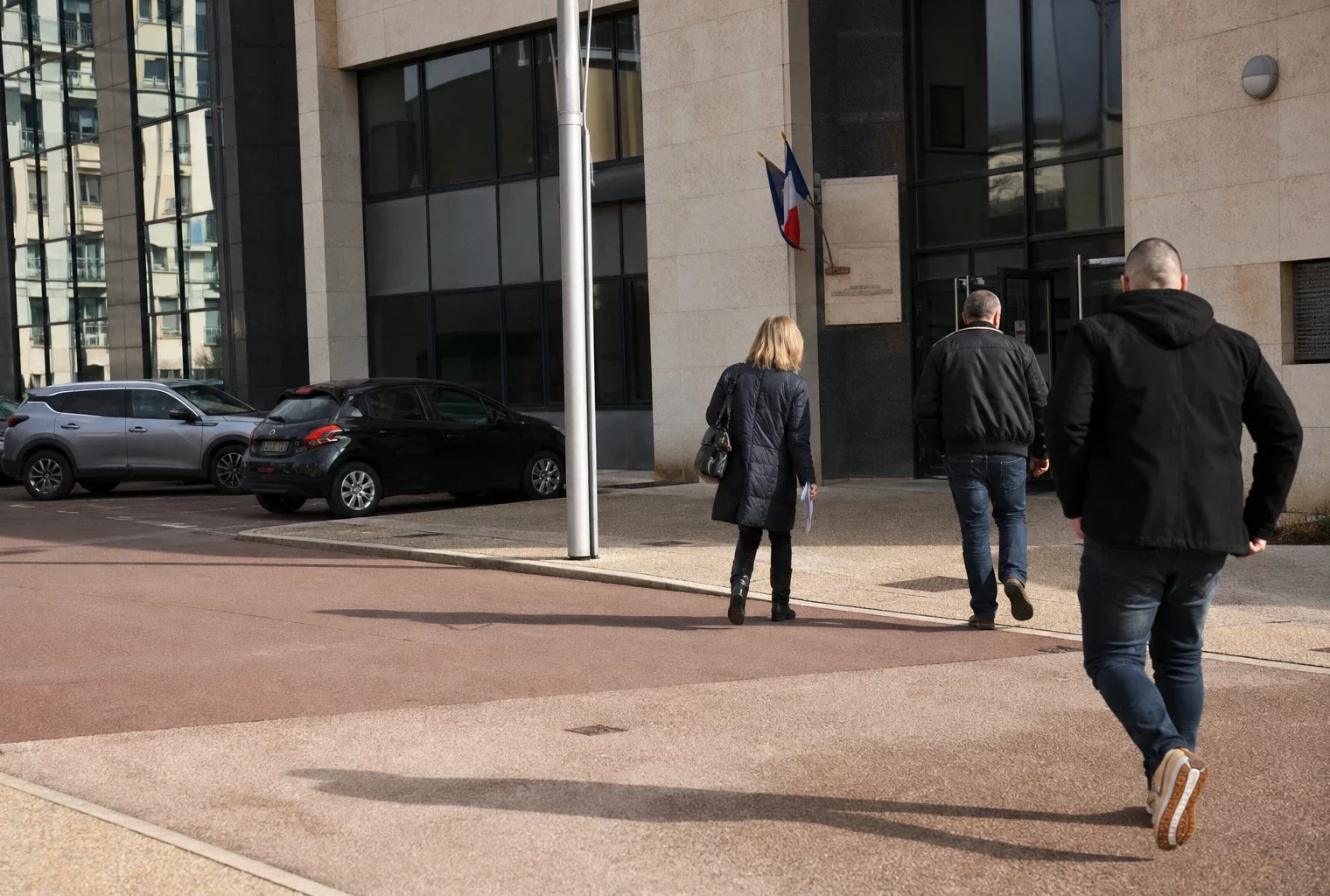 Scène calme devant un bâtiment administratif français, avec agents anonymes, voitures civiles et lumière du jour.