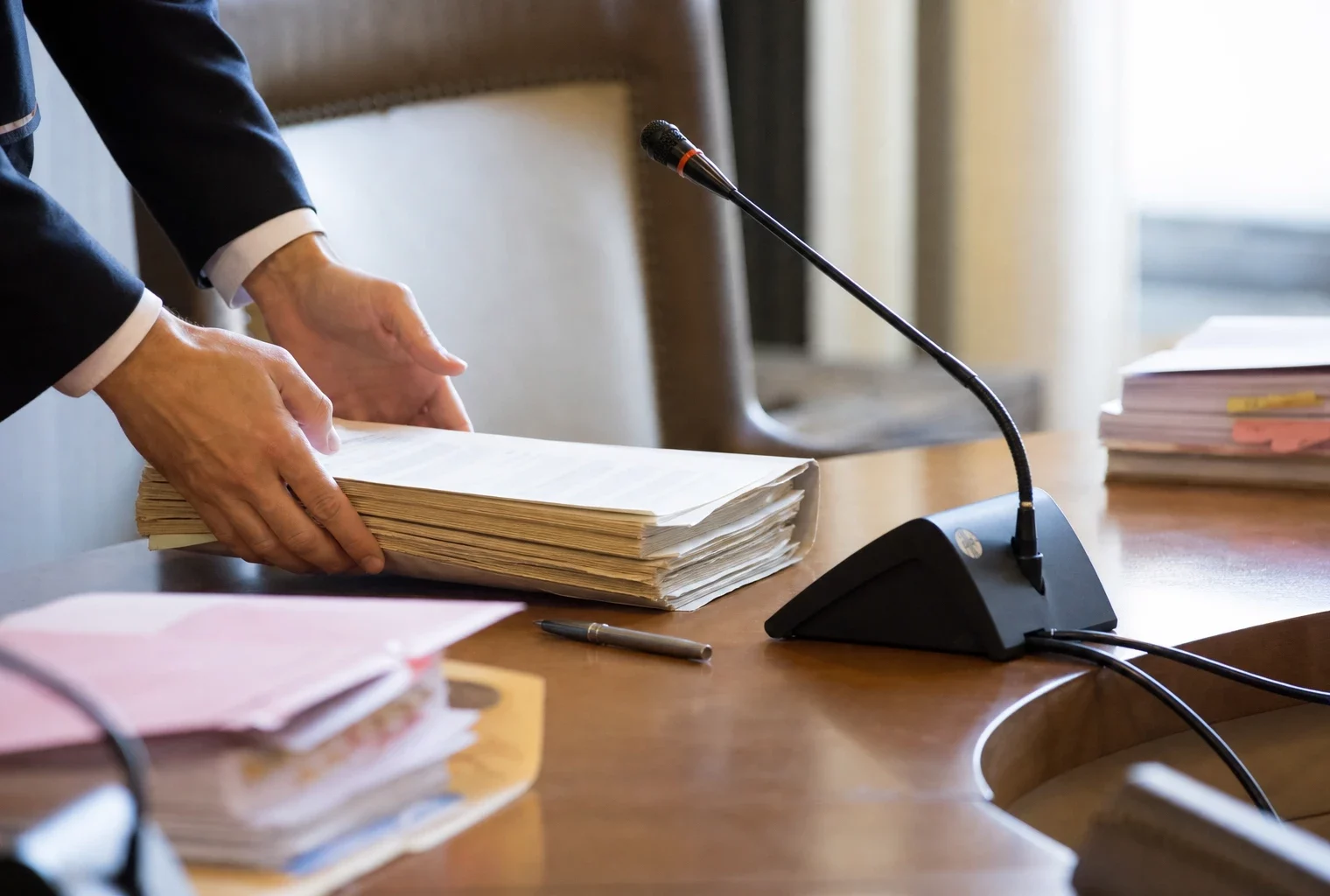 Dossier de commission et micro de table dans un cadre institutionnel français, avec des mains anonymes en gros plan.