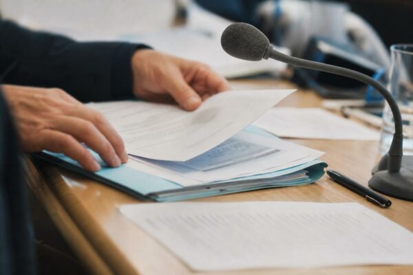 Dossier de commission tenu à la main avec micro de table dans un cadre institutionnel français lumineux