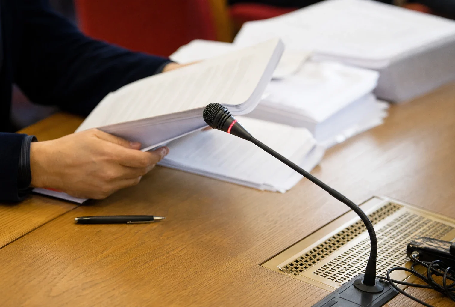 Dossier de commission avec micro de table, mains anonymes et documents flous dans une salle institutionnelle française.